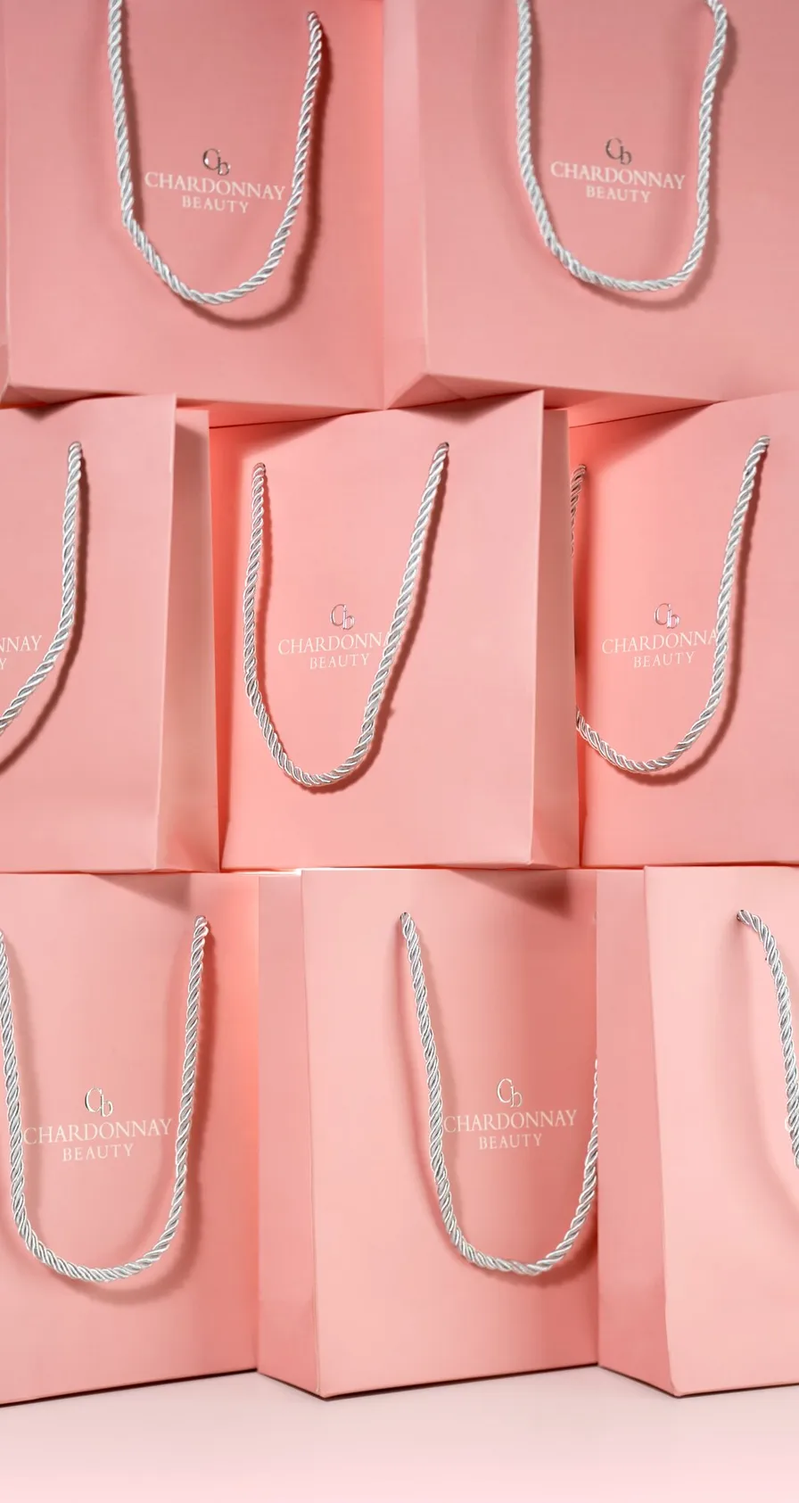 A stack of pink Chardonnay Beauty gift bags with rope handles