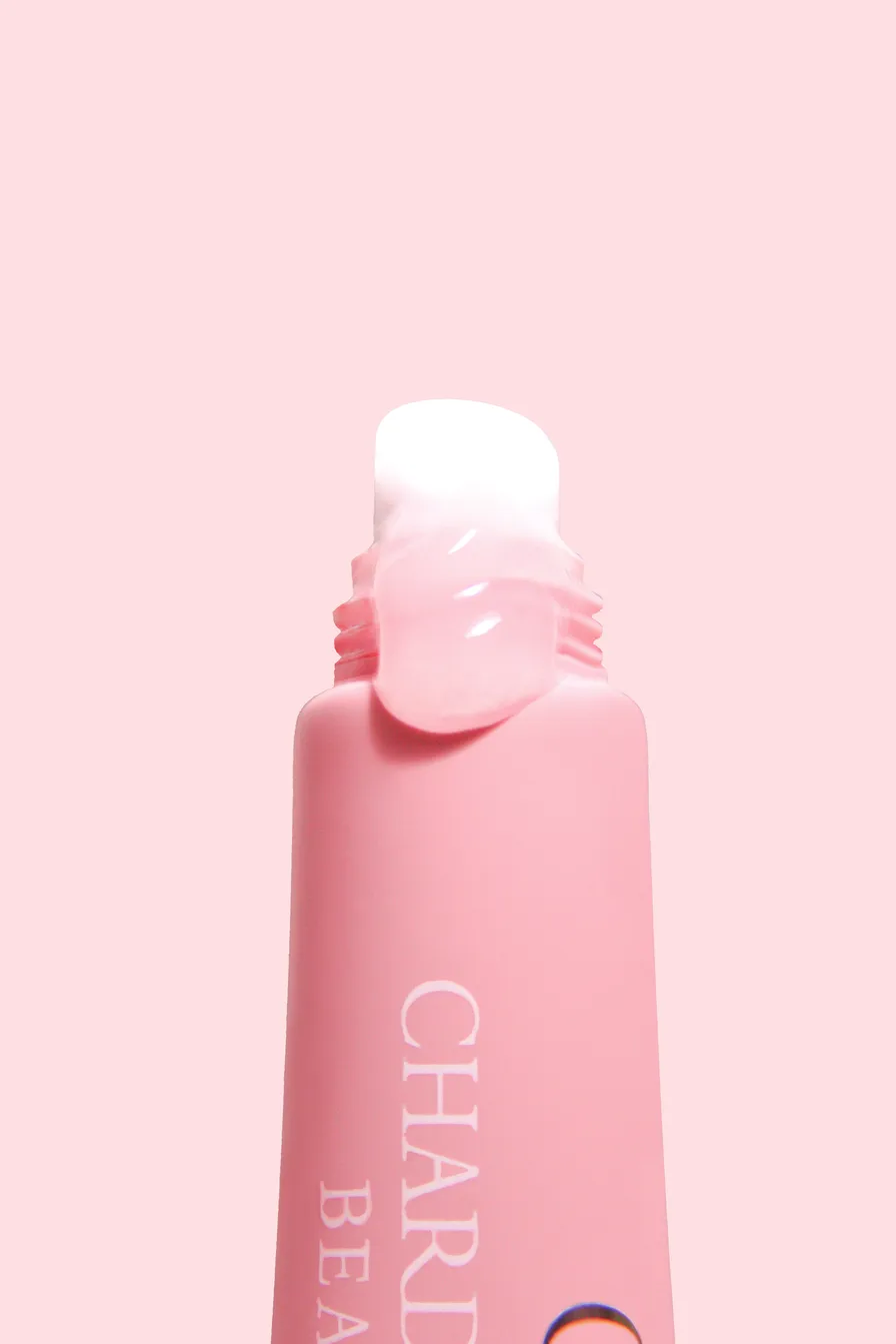 A pink Chardonnay Beauty tube with a clear, glass-like balm swatched over its applicator