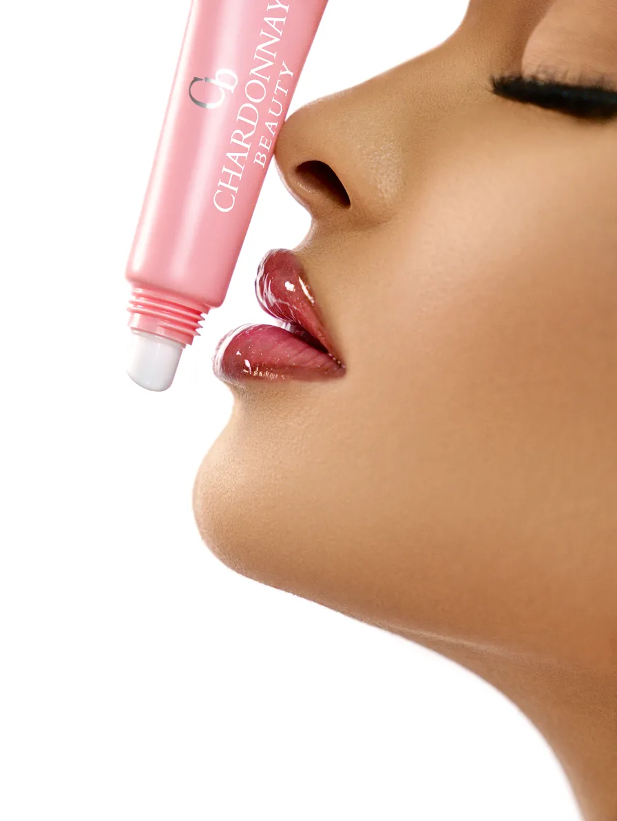 Close profile of lips wearing a sparkling pink gloss, with the Chardonnay Beauty tube held alongside